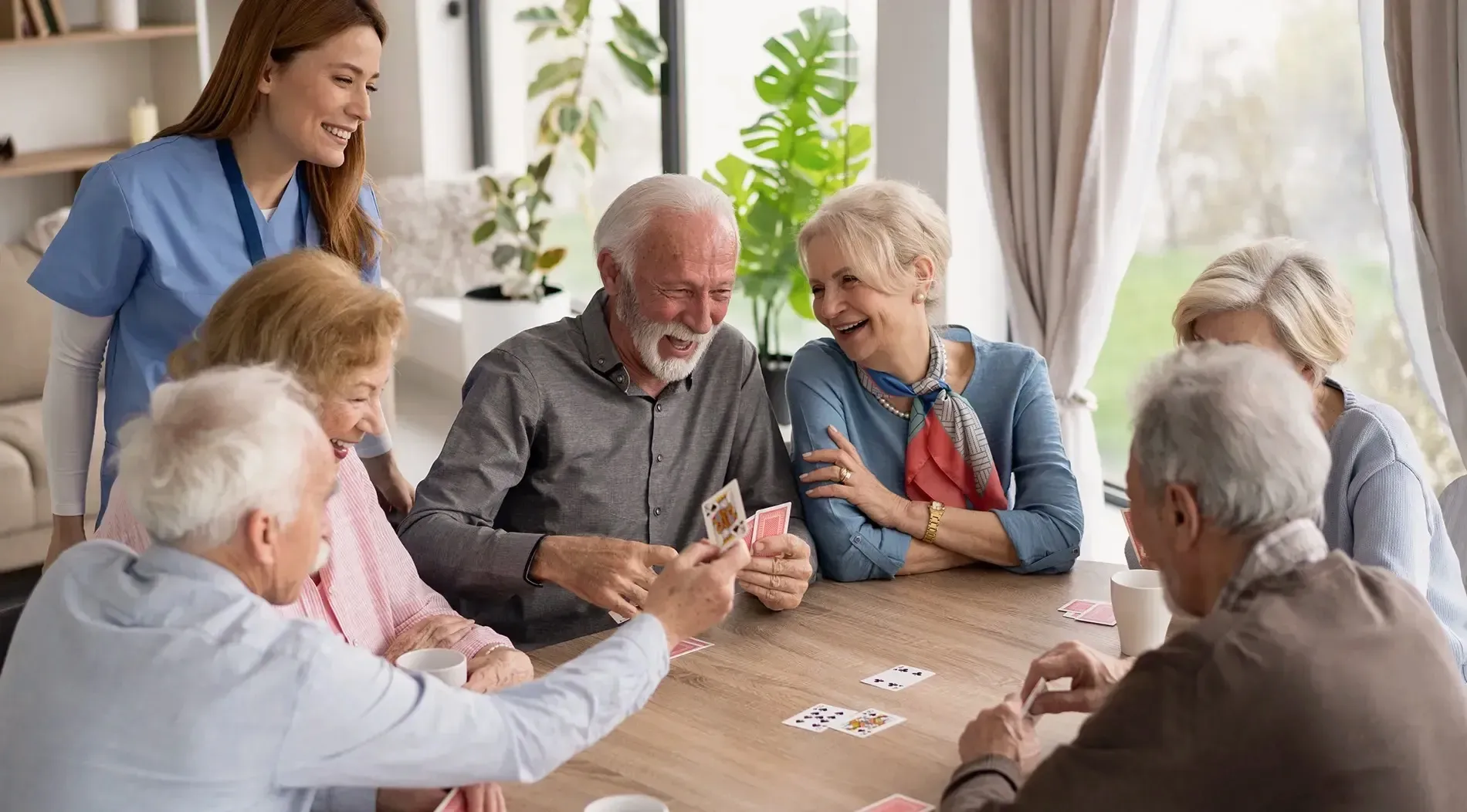 Residents laughing over a card game in a bright assisted living common room