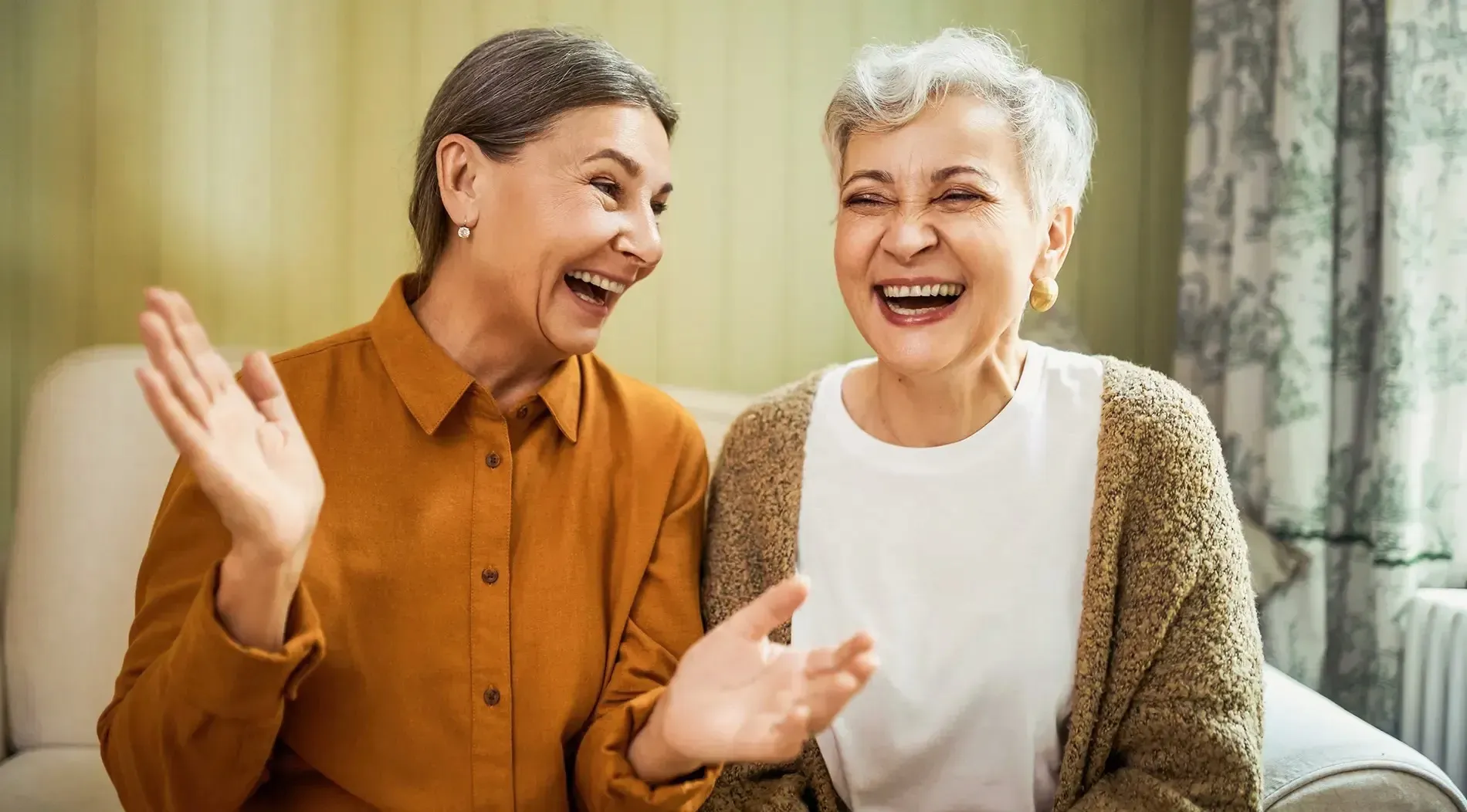 Two women laughing together on a sofa at home