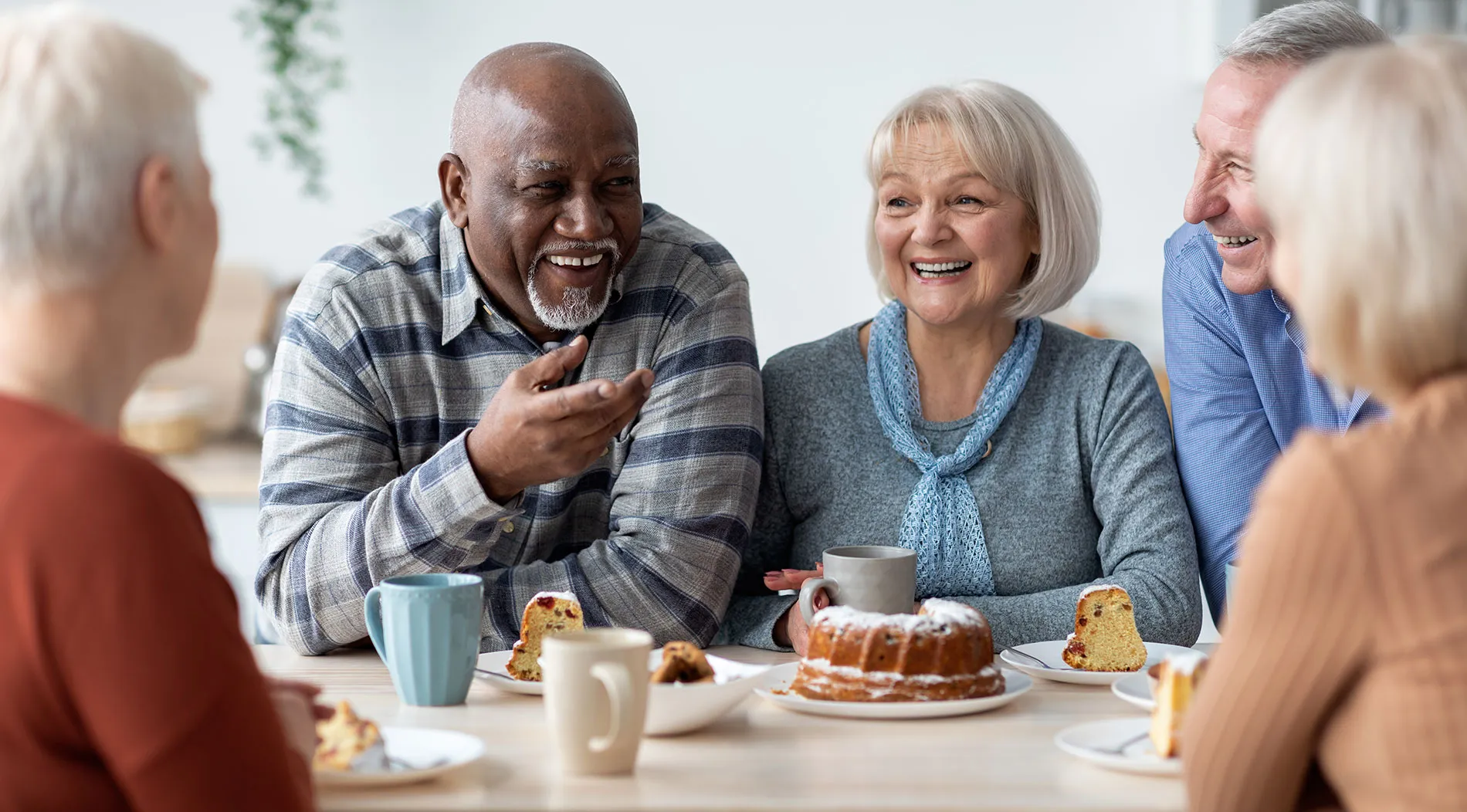 A group of older friends laughing together over coffee and cake